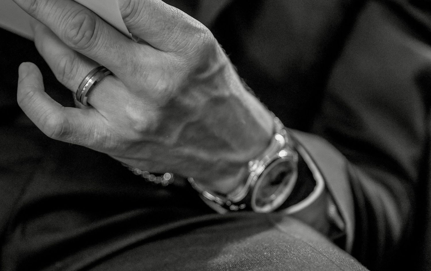 Black and white close-up of a mans hand wearing a ring and bracelet watch.