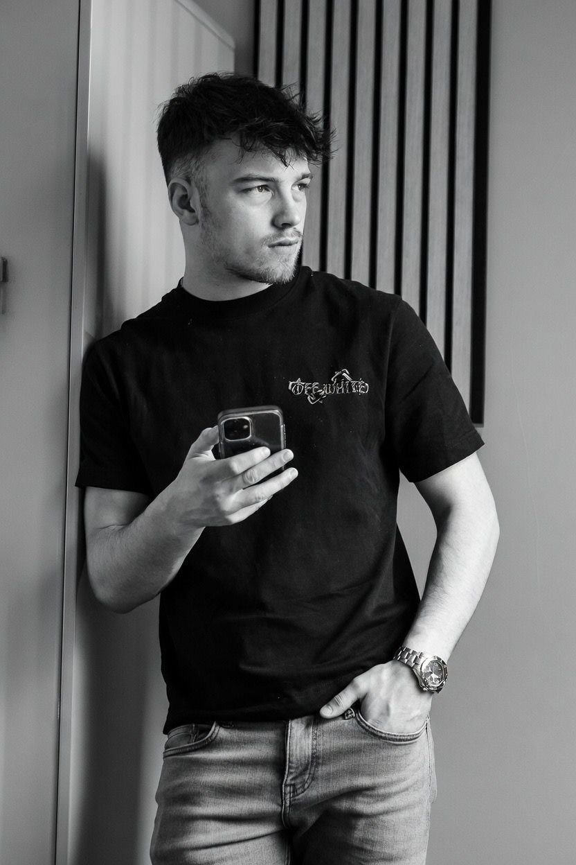 Young man in black t-shirt holding smartphone in black and white portrait photo.