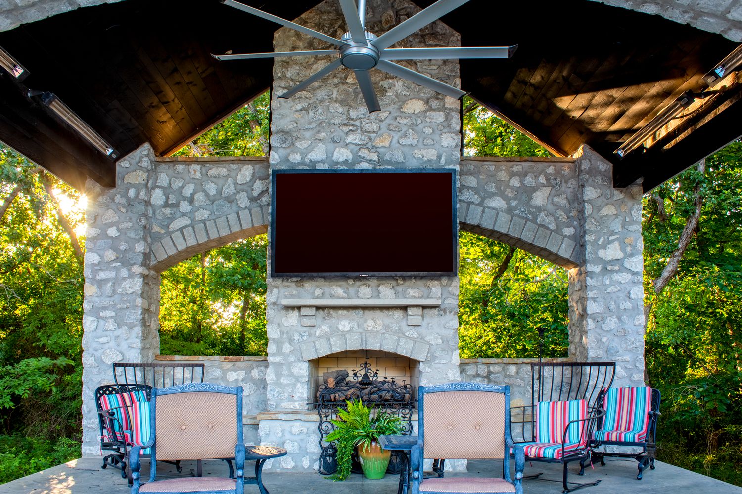 Stone pavilion with ceiling fans and rocking chairs creates a cozy outdoor seating area.