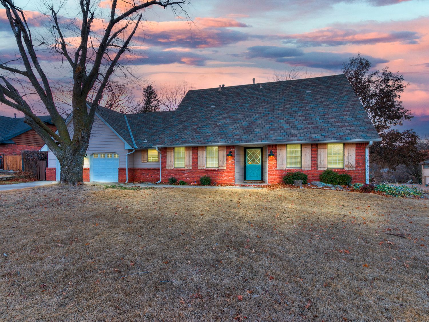 Ranch style home with red brick exterior and teal door captured during a colorful sunset.