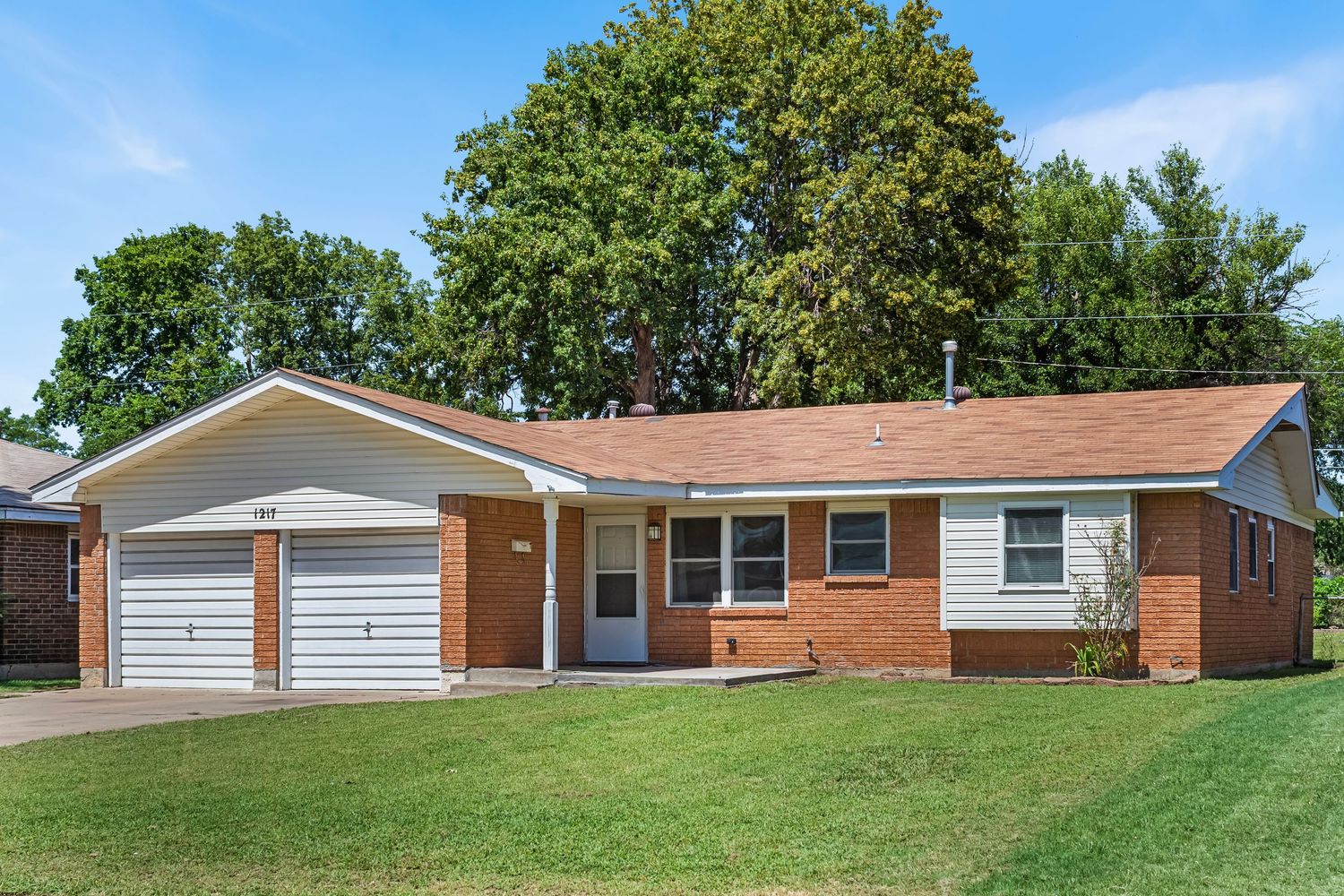 Long view of a single-story brick ranch house with attached garage and well-maintained lawn.