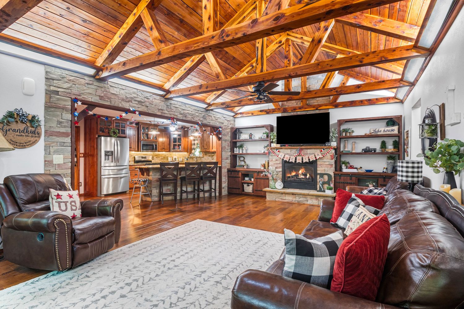 Rustic living room with exposed wooden beams, stone fireplace, and leather furniture under vaulted ceilings.