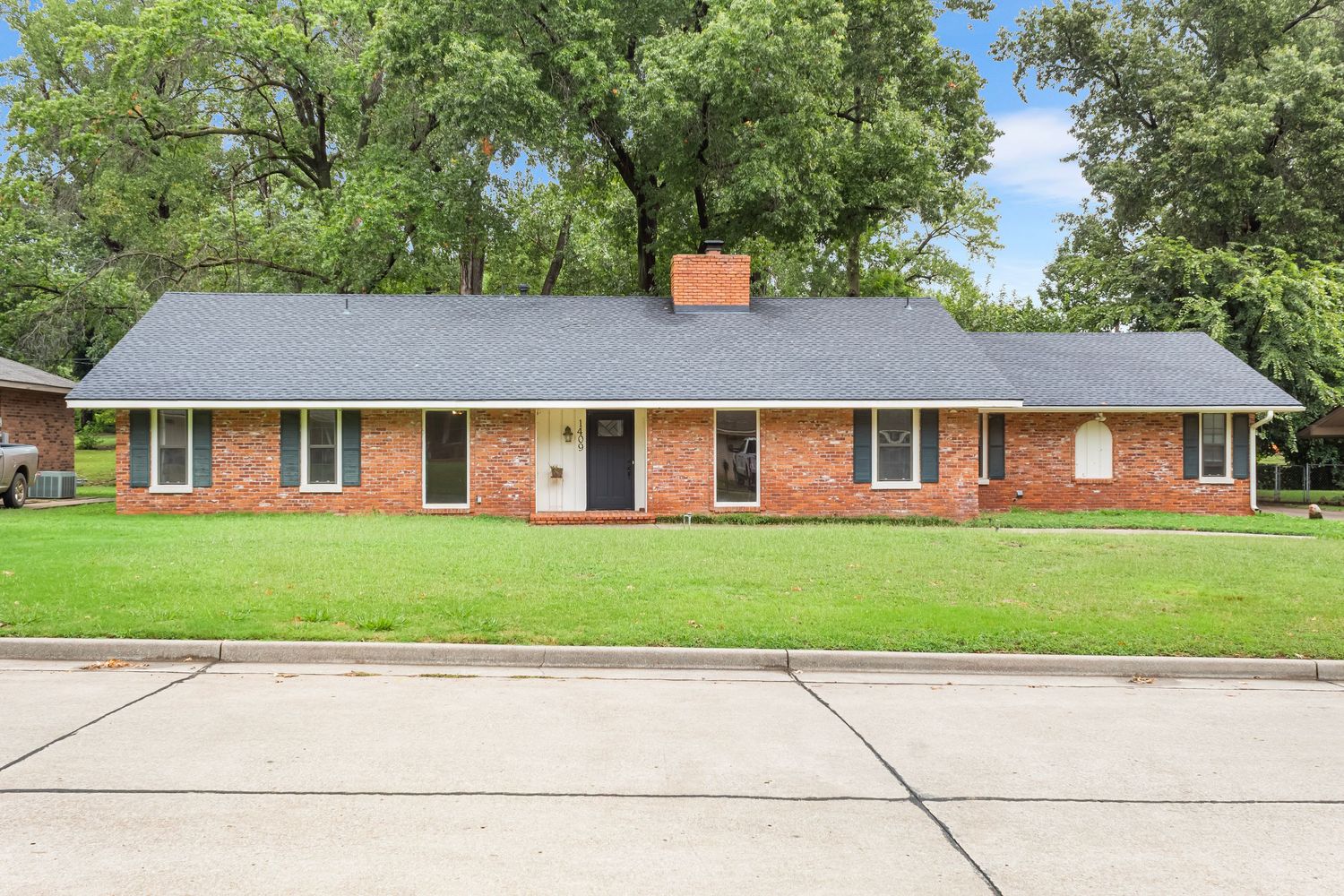 Panoramic view of a brick ranch house with wide driveway and expansive front lawn.