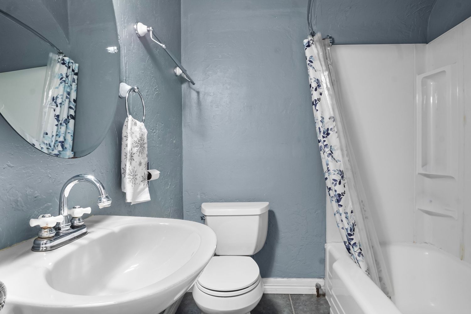 Modern bathroom with blue-gray walls, white fixtures, and floral shower curtain.