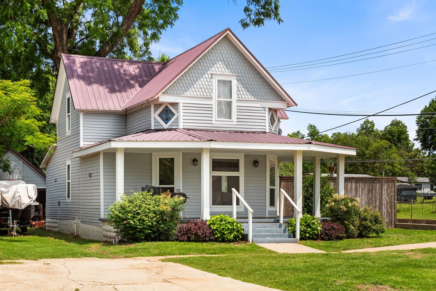 Exterior view of a ranch-style home with white siding and pink trim surrounded by green landscaping.