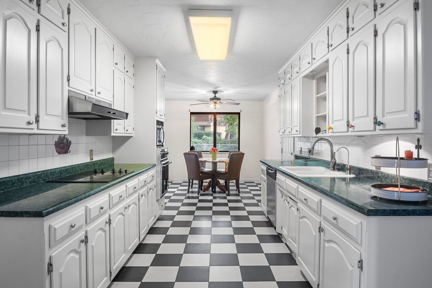Modern white kitchen with black and white checkered floor and extensive cabinet storage.
