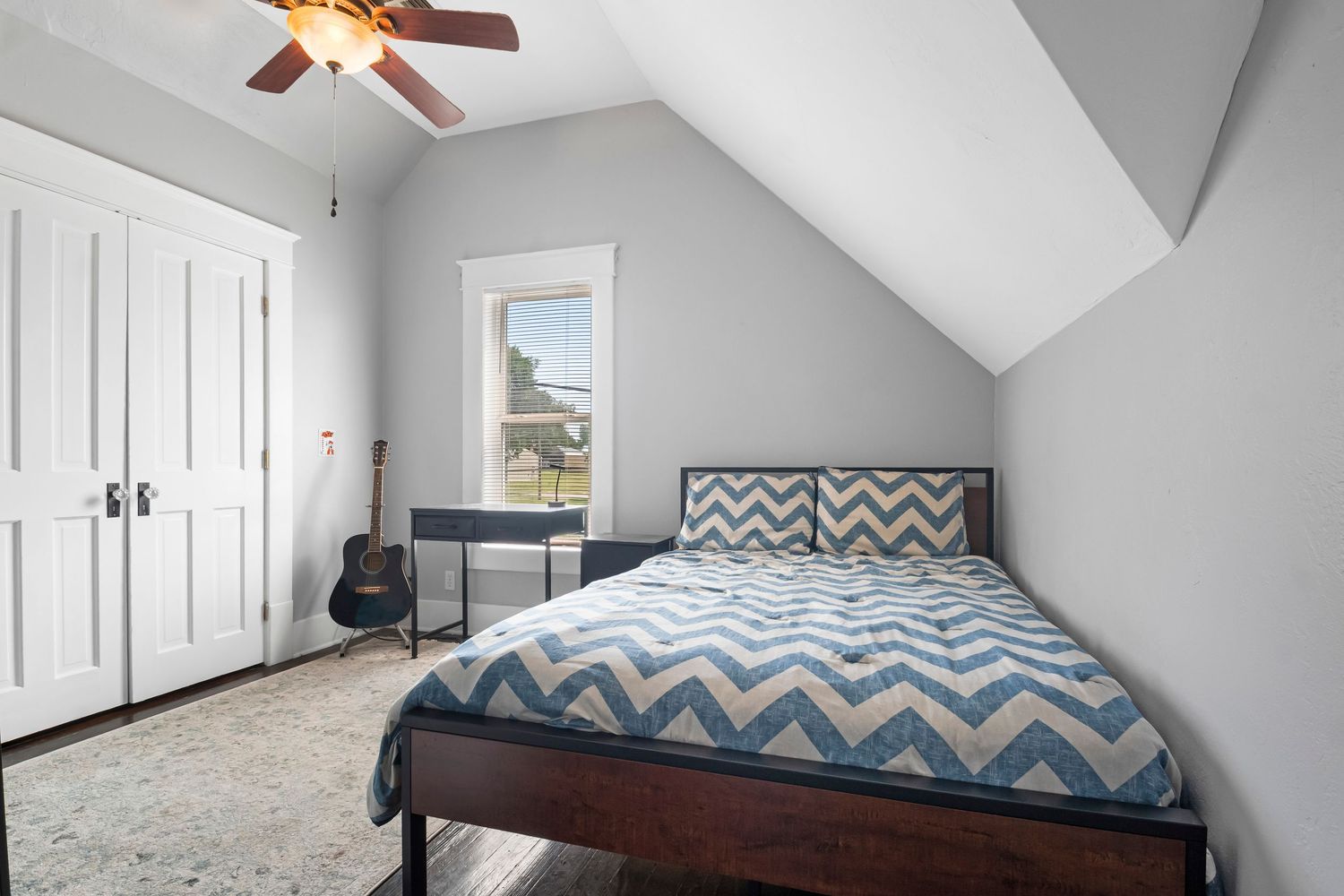 Cozy bedroom with chevron bedding under sloped ceiling featuring built-in closets and hardwood floors.