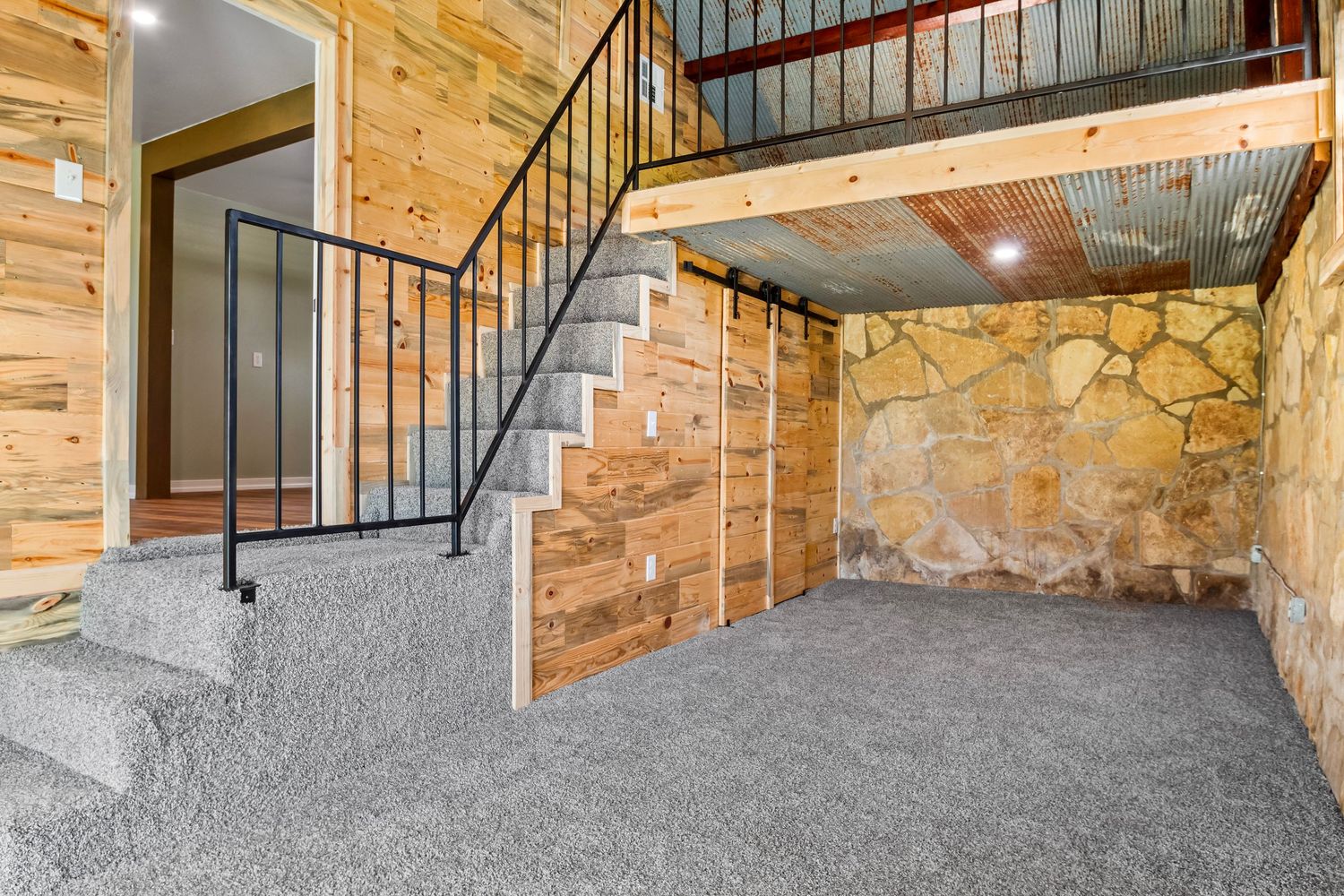 Basement entrance with wooden walls, metal railing staircase, and gray carpeted floor.