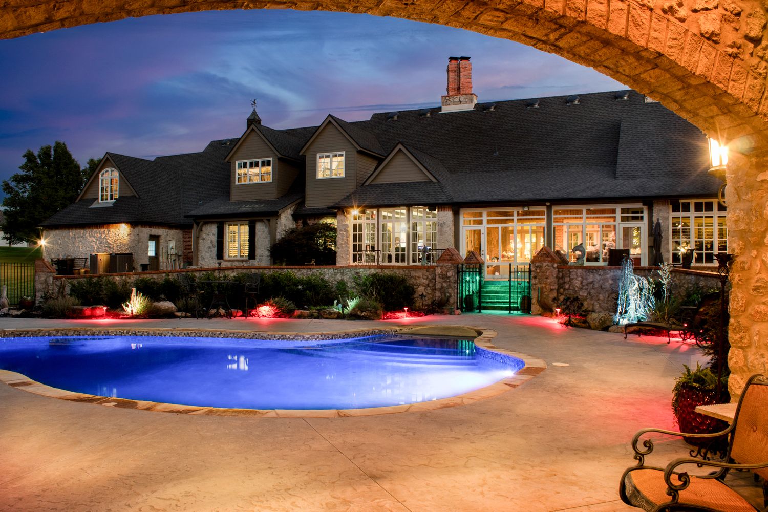 Large swimming pool illuminated at night with ambient lighting and surrounding patio space.