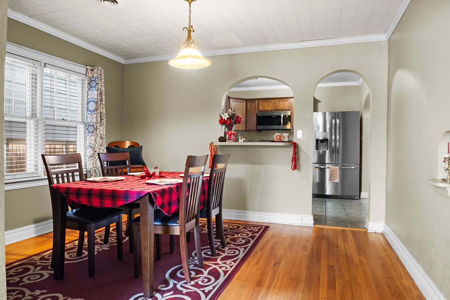 Dining room with wooden floors, red tablecloth, and arched doorway leading to kitchen.
