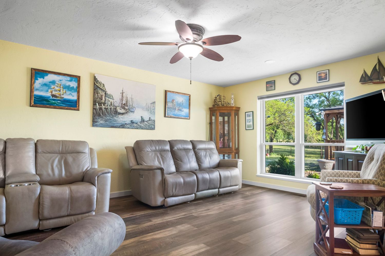 Living room with reclining leather furniture, hardwood floors, and coastal artwork on yellow walls.