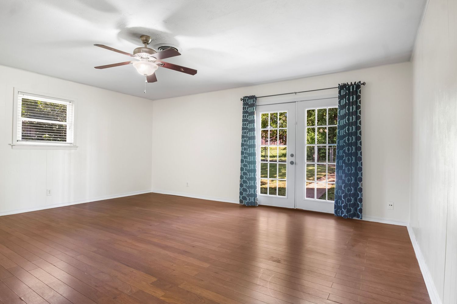 Spacious empty room with hardwood floors, white walls, and large windows with natural light.