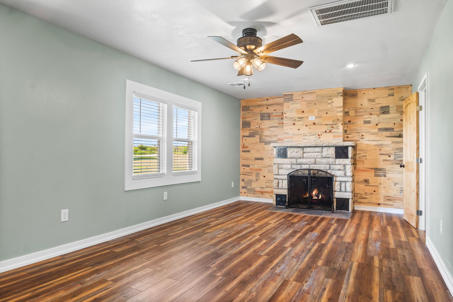 Spacious room with hardwood floors, ceiling fan, and exposed brick accent wall.