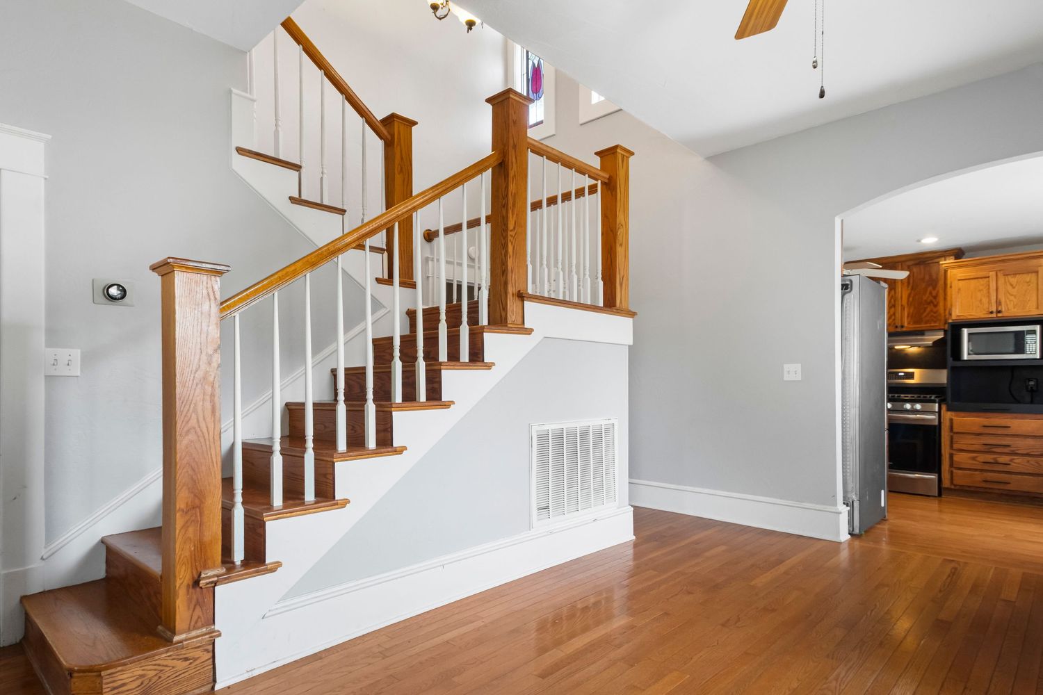 Modern wooden staircase with white spindles and warm hardwood flooring in an open foyer area.
