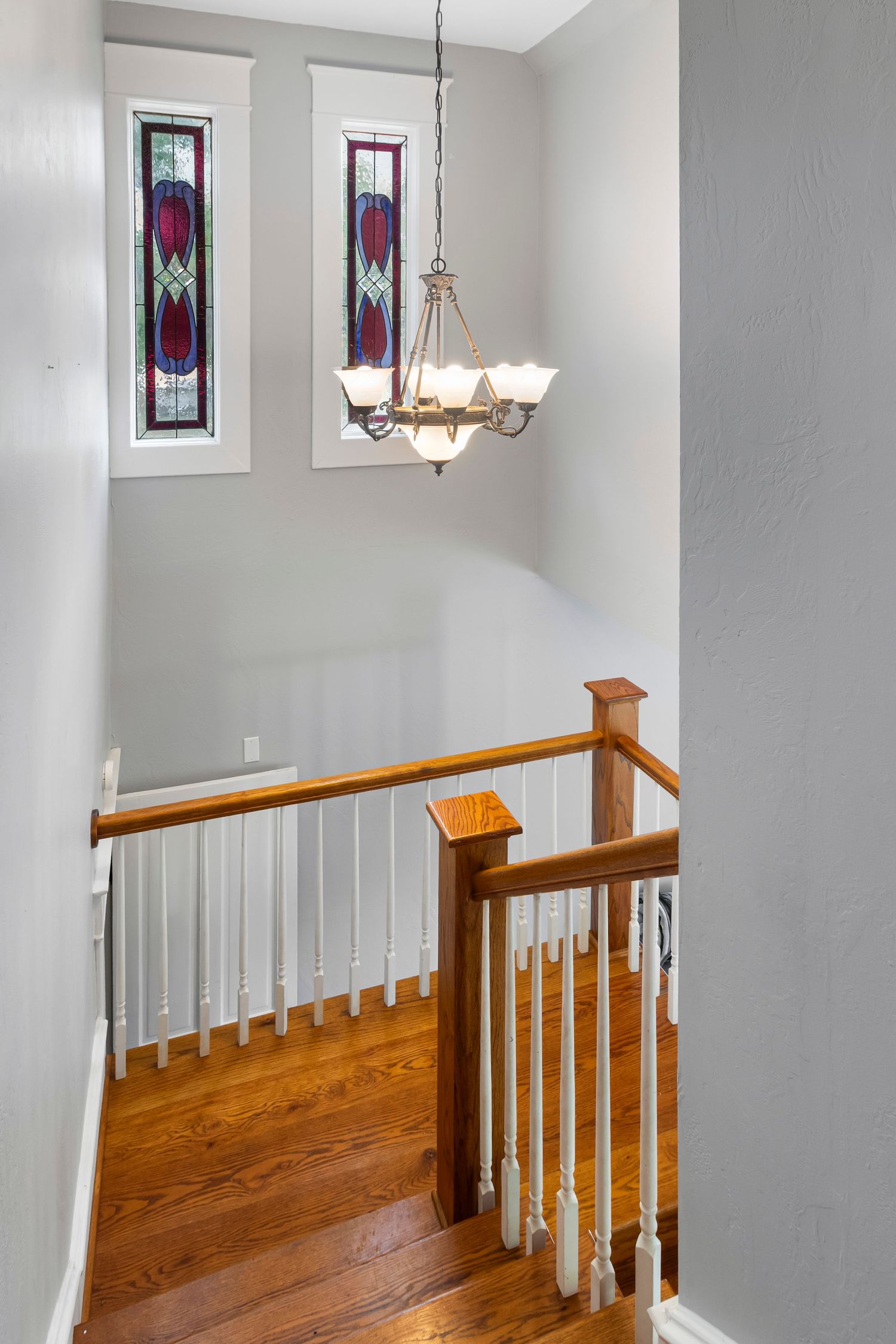 Upstairs hallway with wooden banister and decorative stained glass windows.