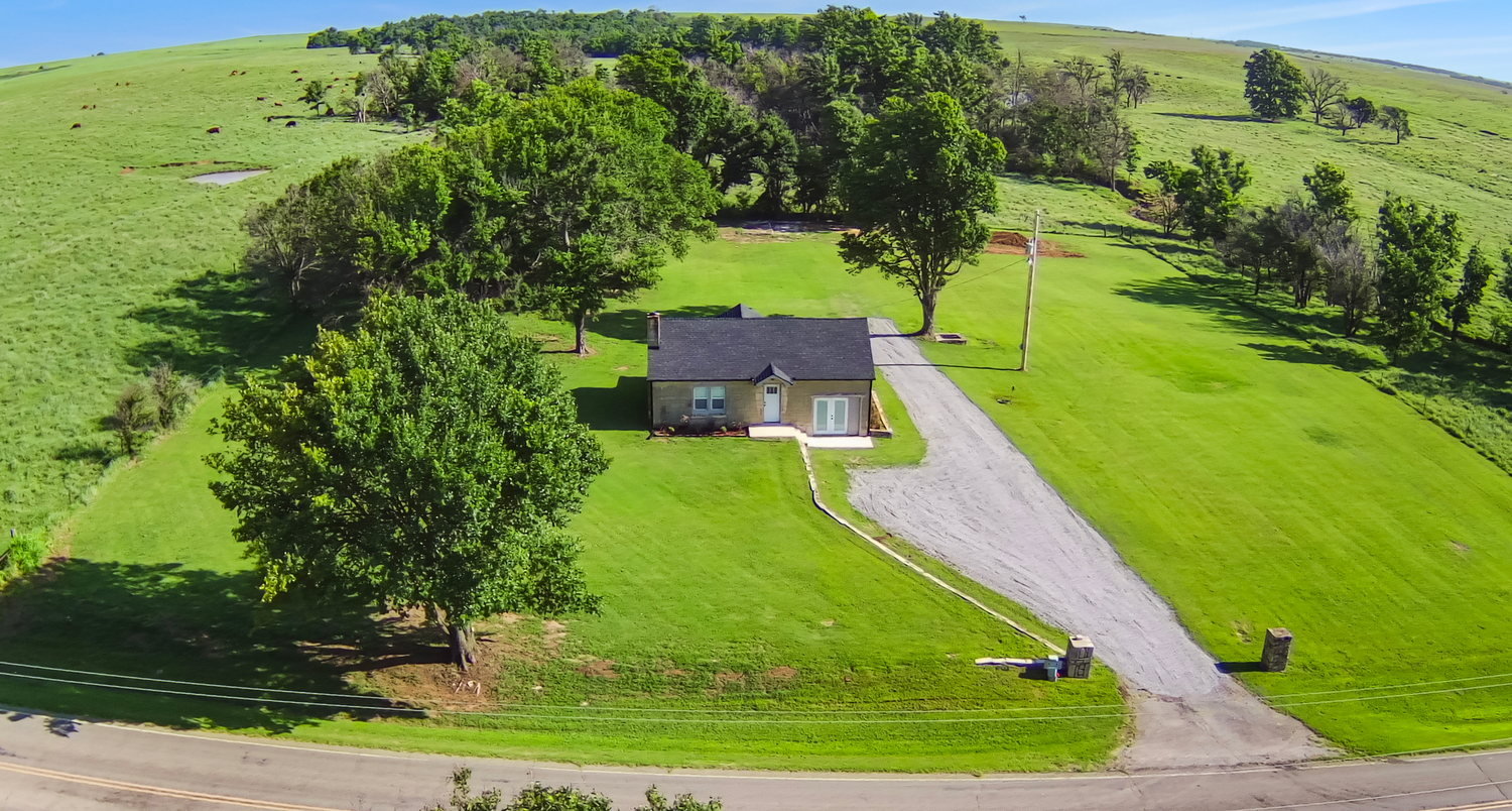 Aerial view of a ranch home surrounded by green rolling hills and mature trees.