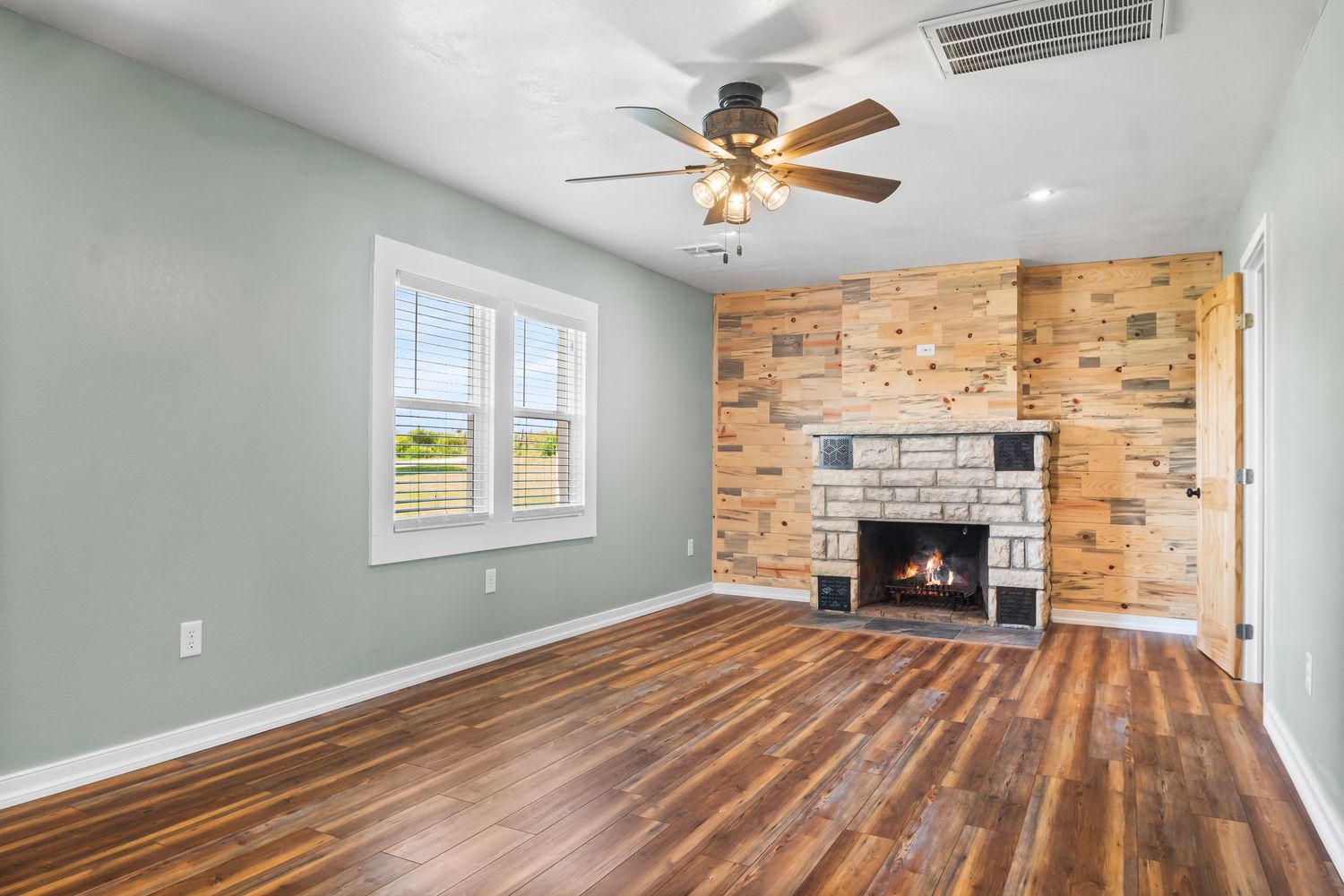 Bright room with hardwood floors, mint green walls, and brick fireplace beneath ceiling fan.