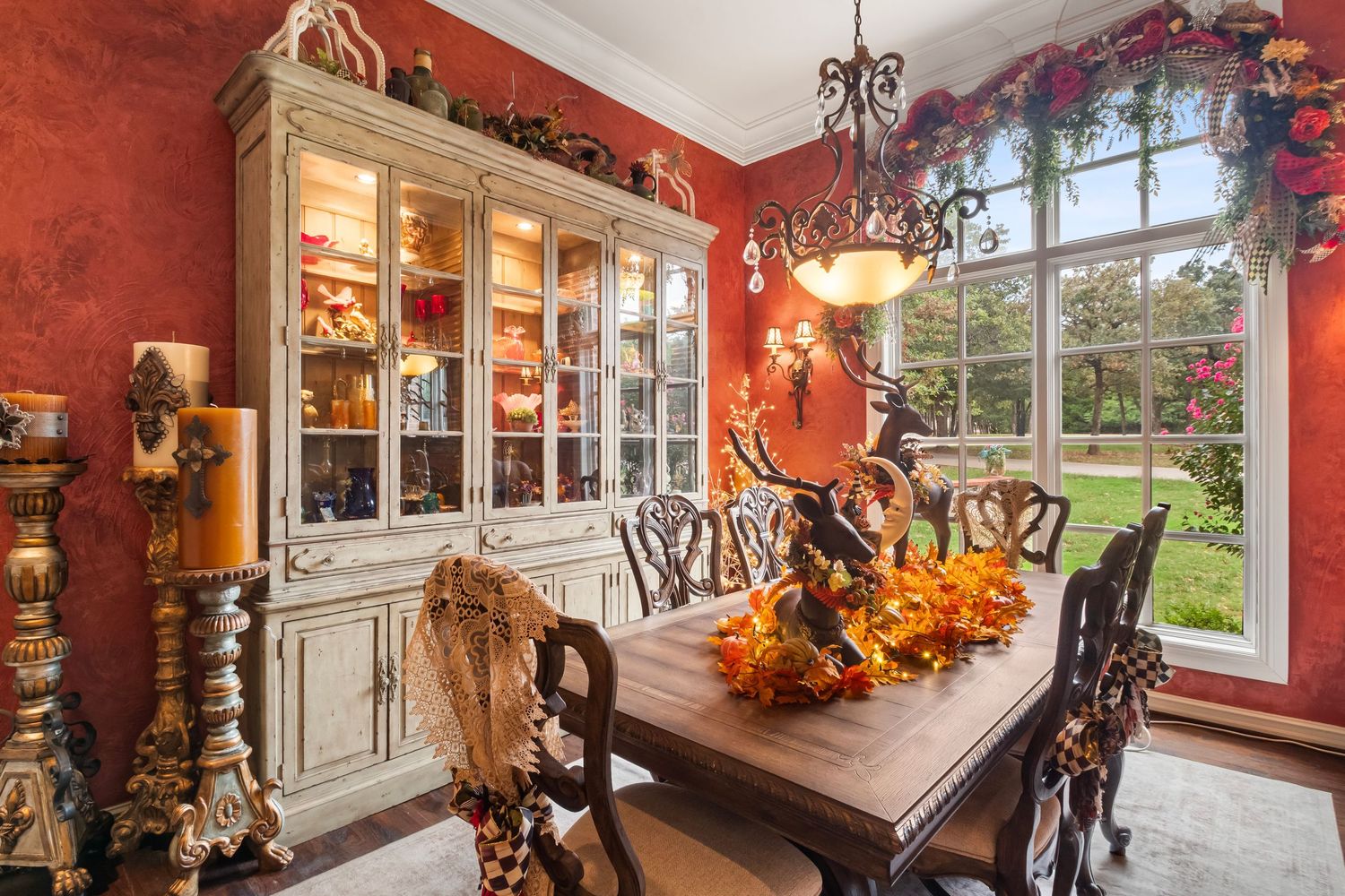 Red dining room with large windows, chandelier, and seasonal fall decorations.