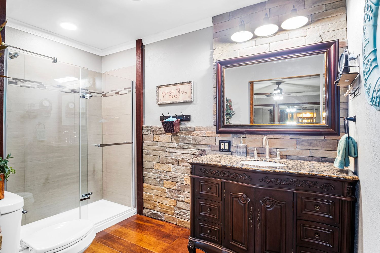 Modern bathroom featuring glass shower, stone accent wall, and dark wood vanity with framed mirror.
