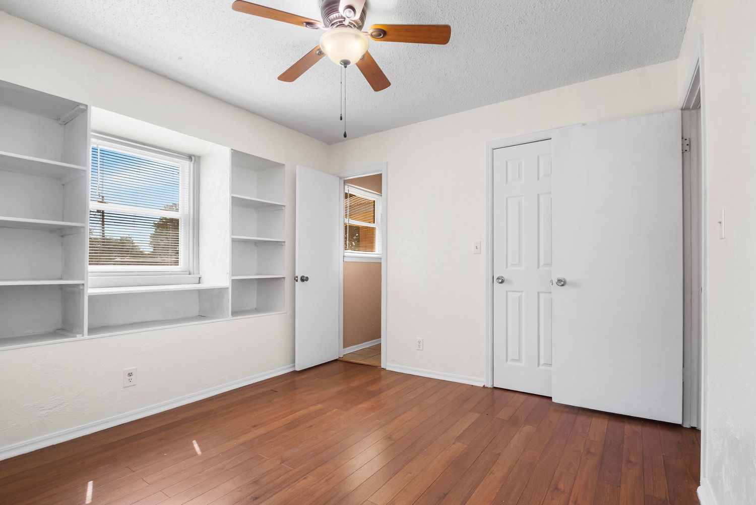 Large bedroom with hardwood flooring, ceiling fan, and built-in white shelving units.