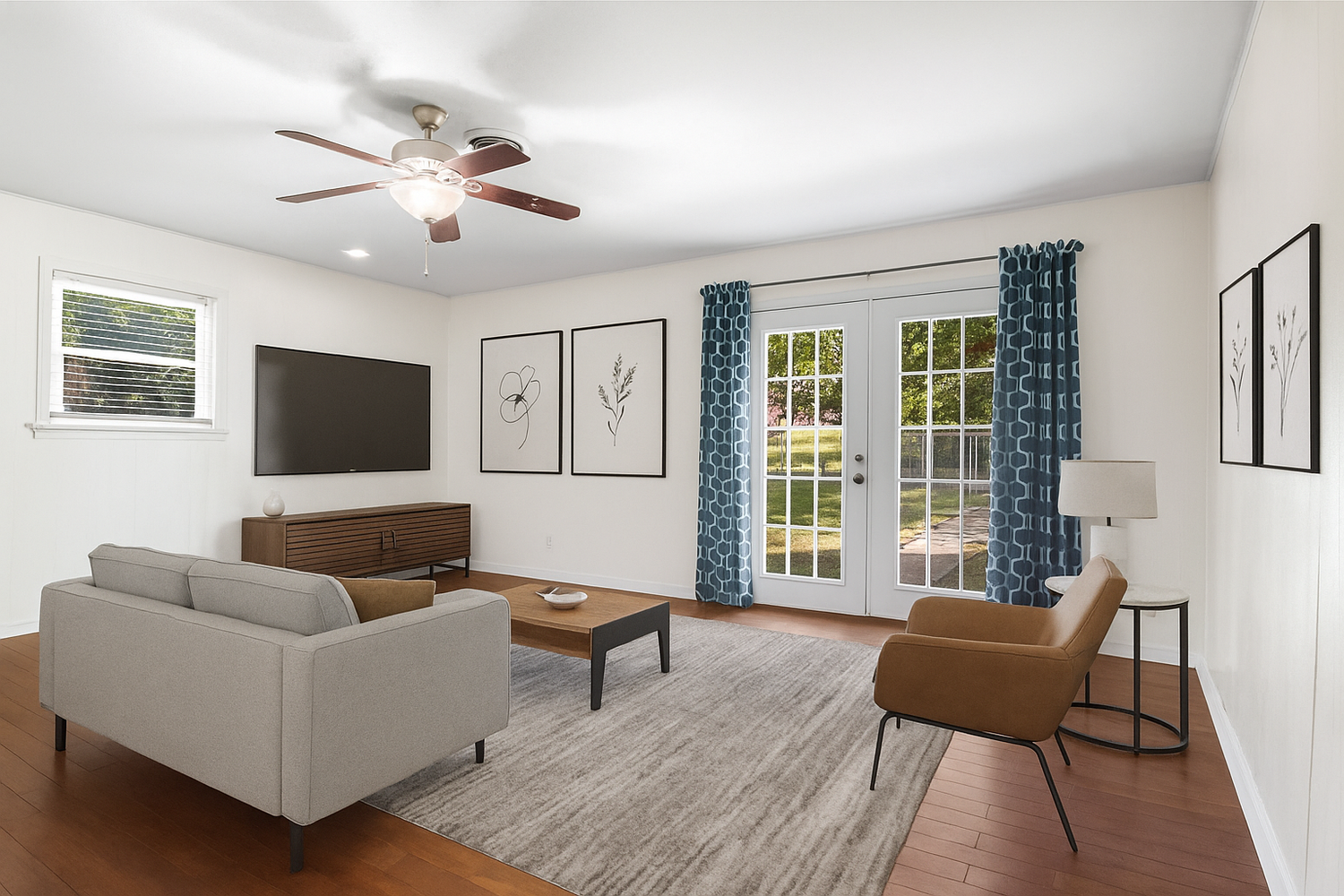 Modern living room with ceiling fan, French doors, brown furniture, and hardwood flooring.