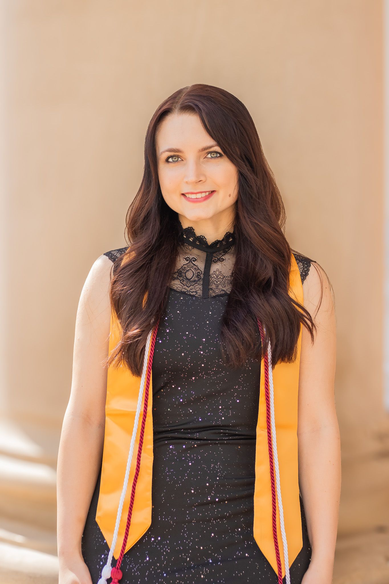 Professional portrait of someone wearing a black sleeveless top and orange safety vest against a beige background.