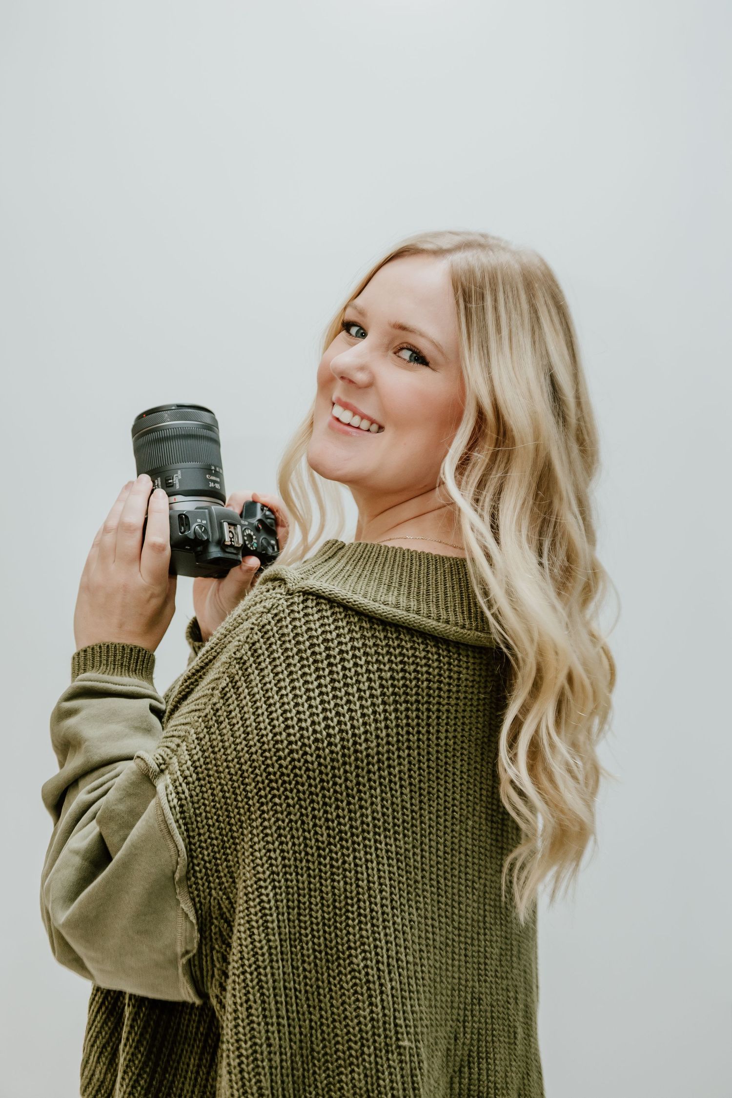 A person in an olive green knit sweater poses and smiles while holding a camera in three sequential photos.