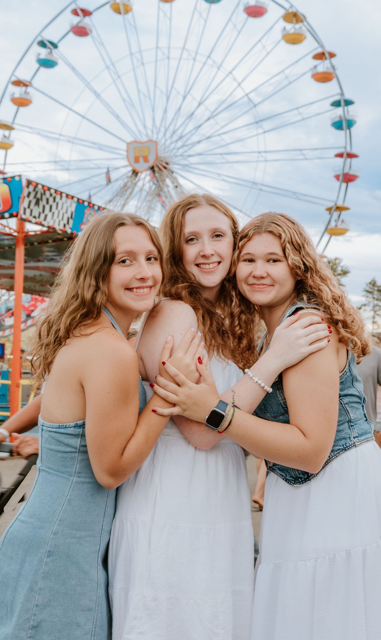 A group of friends share joyful moments at an amusement park with a Ferris wheel visible in the background.
