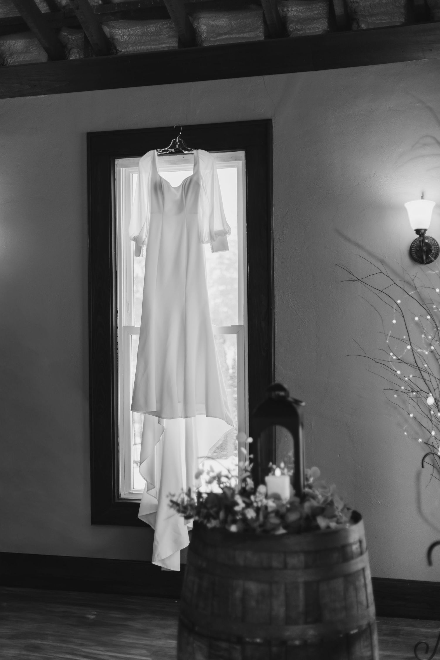 A black and white photo series showing white dresses hanging near windows with rustic wooden barrels and floral decor.