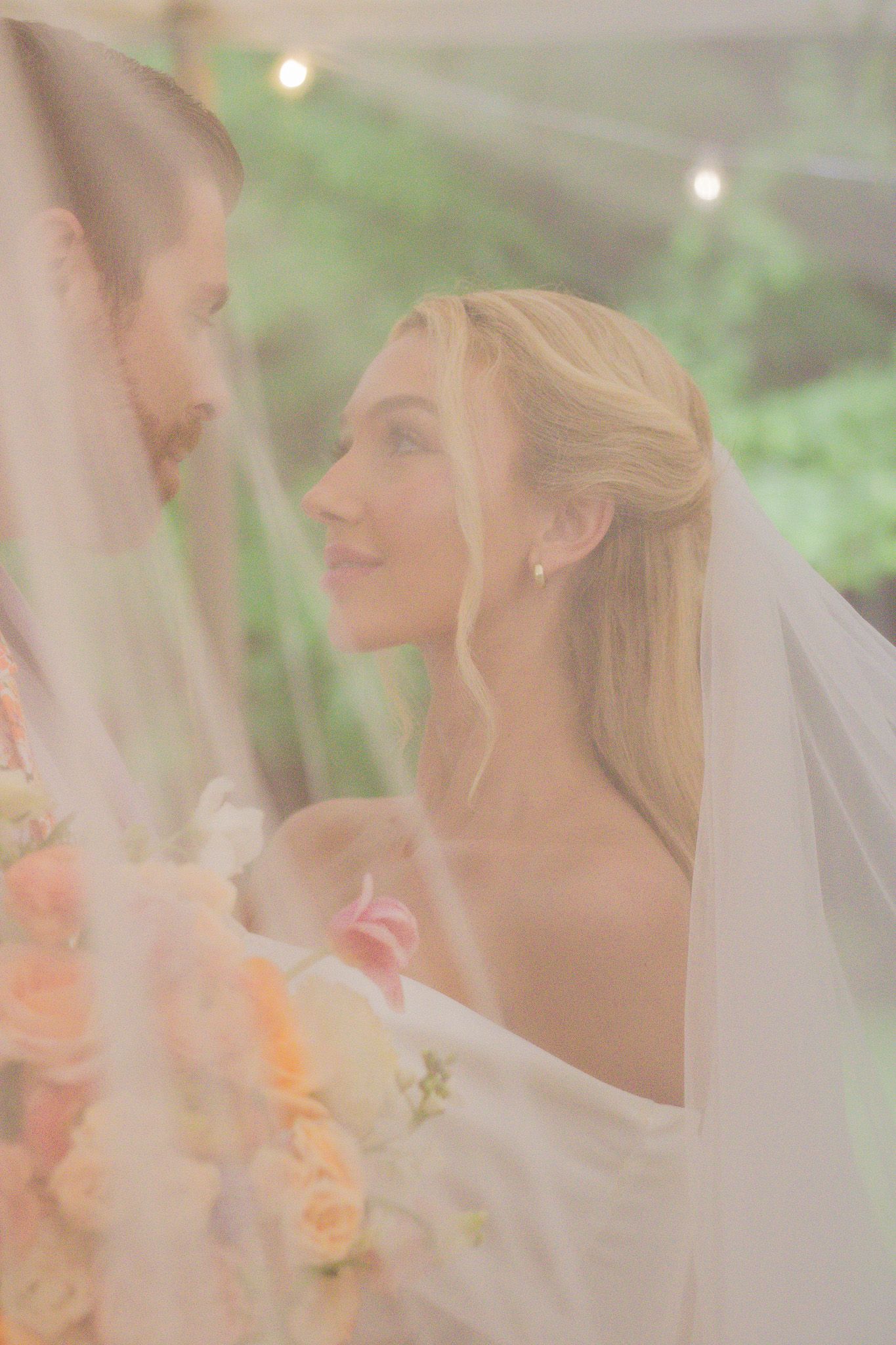 A romantic wedding portrait shows a couple in soft focus with peach-colored flowers and a flowing white veil.