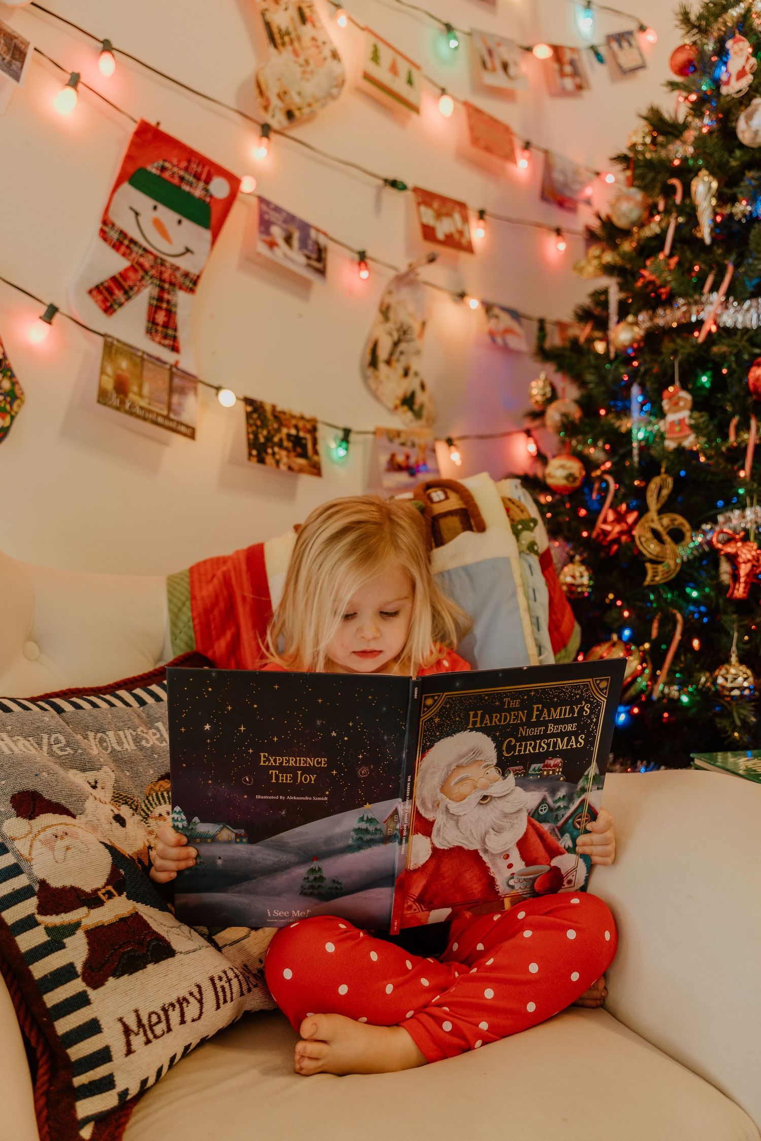 A cozy Christmas reading nook with string lights, photos, and books arranged on a white couch near a decorated tree.