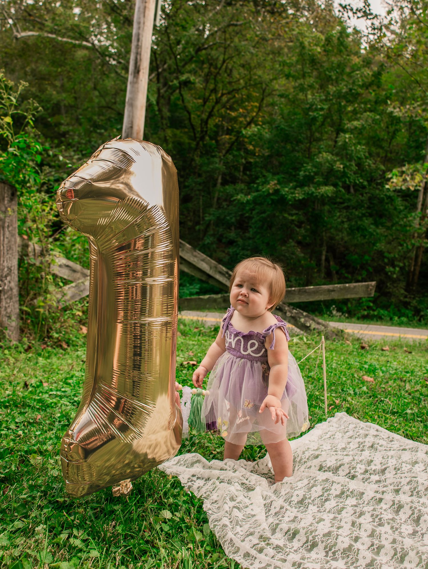 Baby sitting on white lace blanket with gold number 2 balloon decoration.