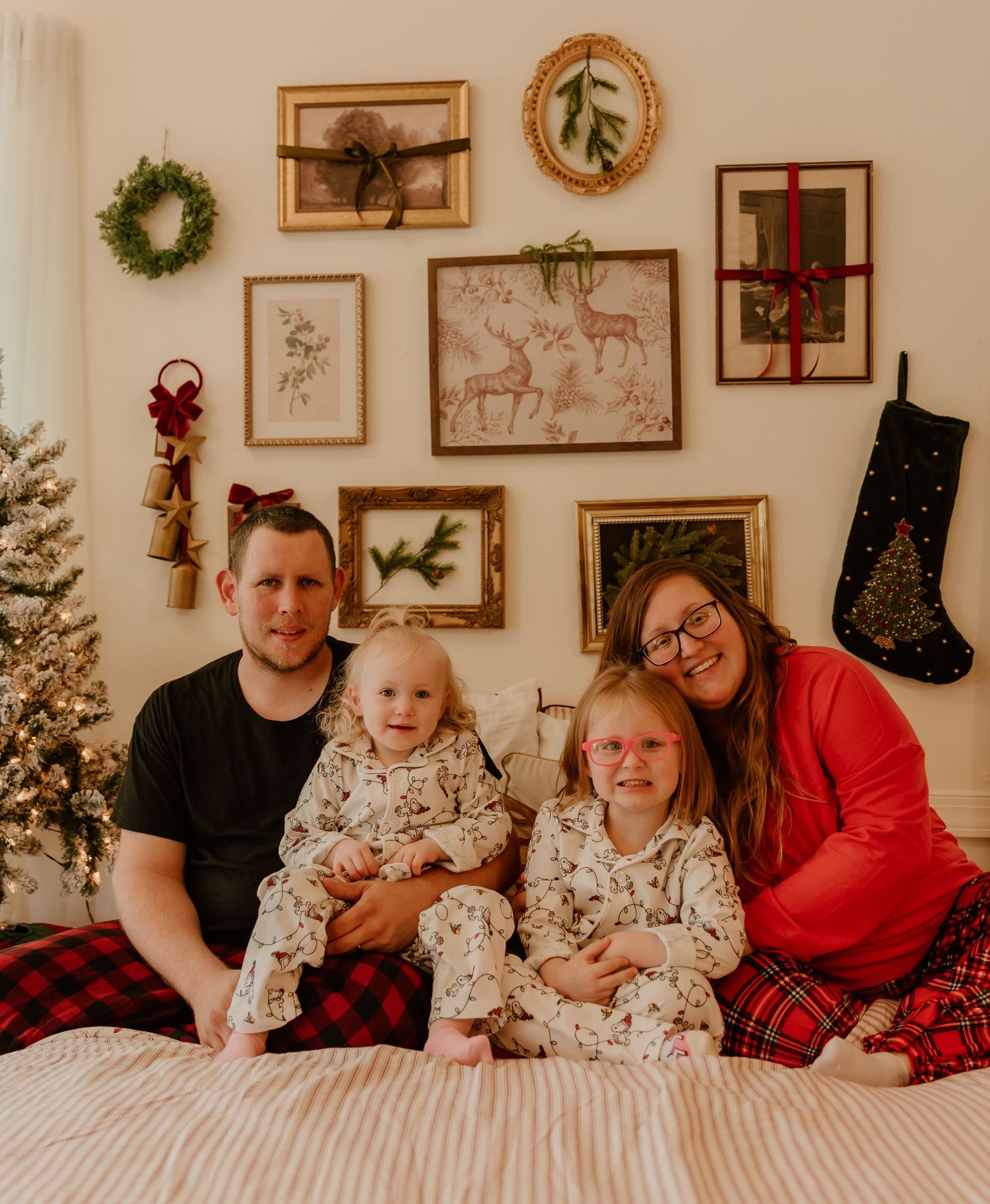 Family lounging on bed in matching holiday pajamas with festive wall decor and Christmas decorations in background.