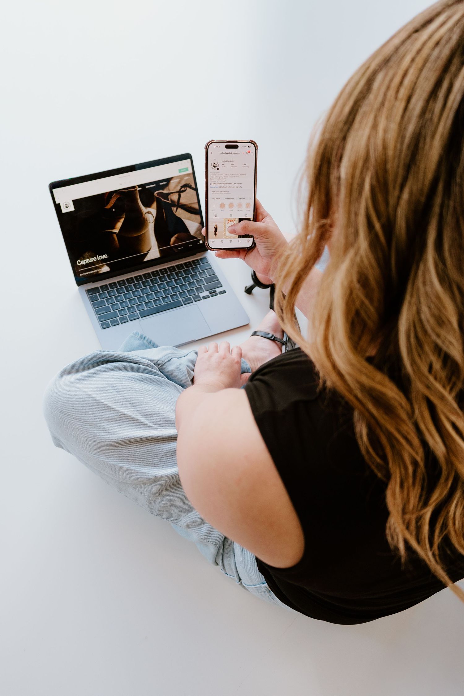 Person working on laptop and mobile phone while sitting on floor showing modern remote work setup.