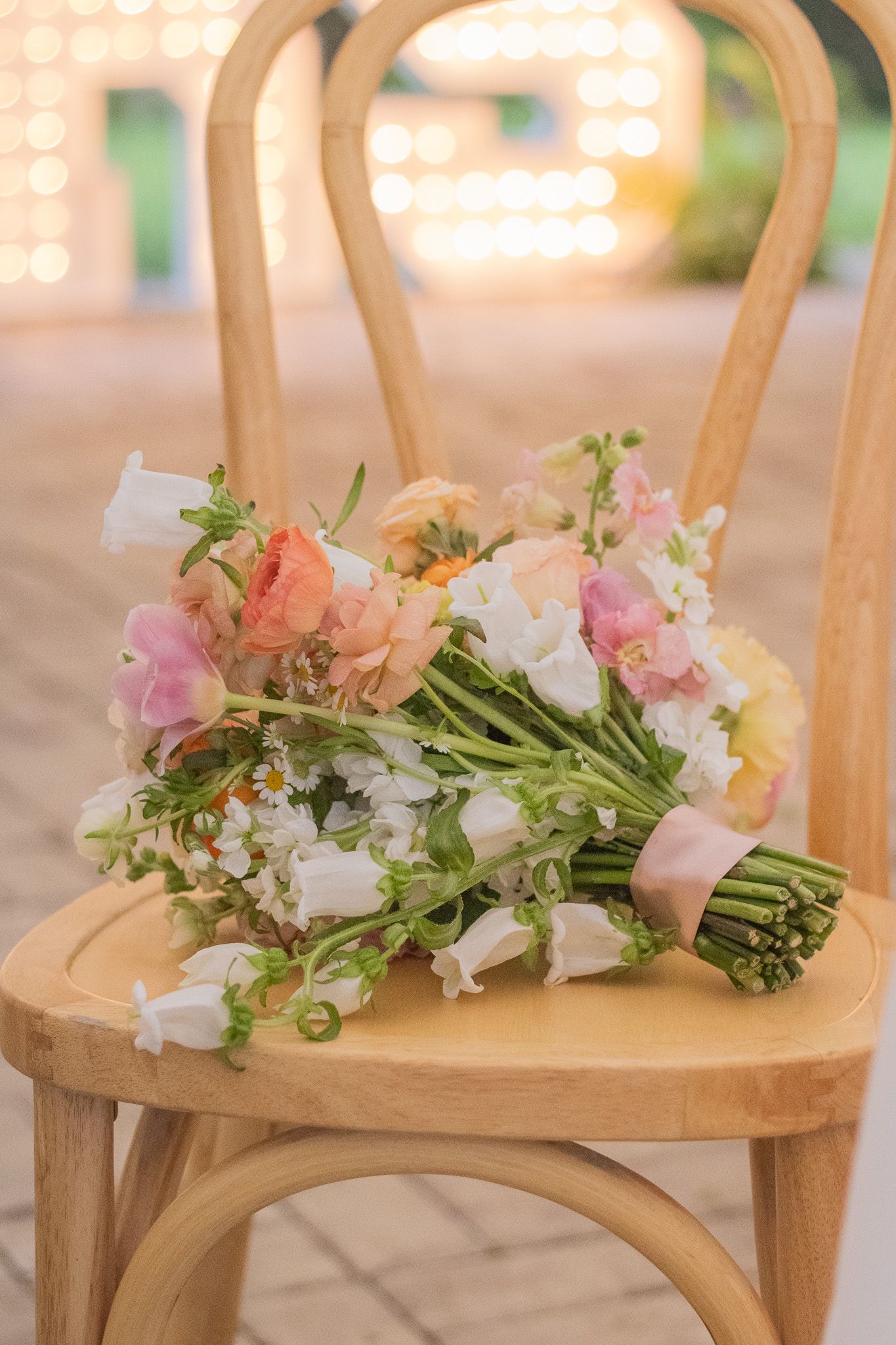 Delicate pink and white floral arrangements rest on wooden chairs in an elegant outdoor setting.