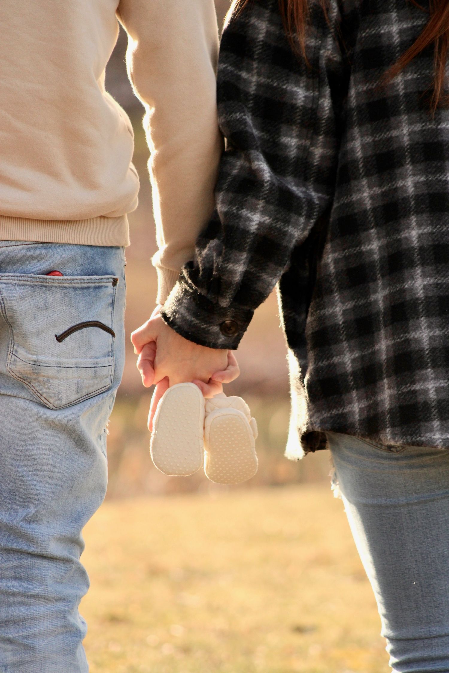 Silhouetted couple holding hands against golden sunlight while wearing plaid shirt and jeans.