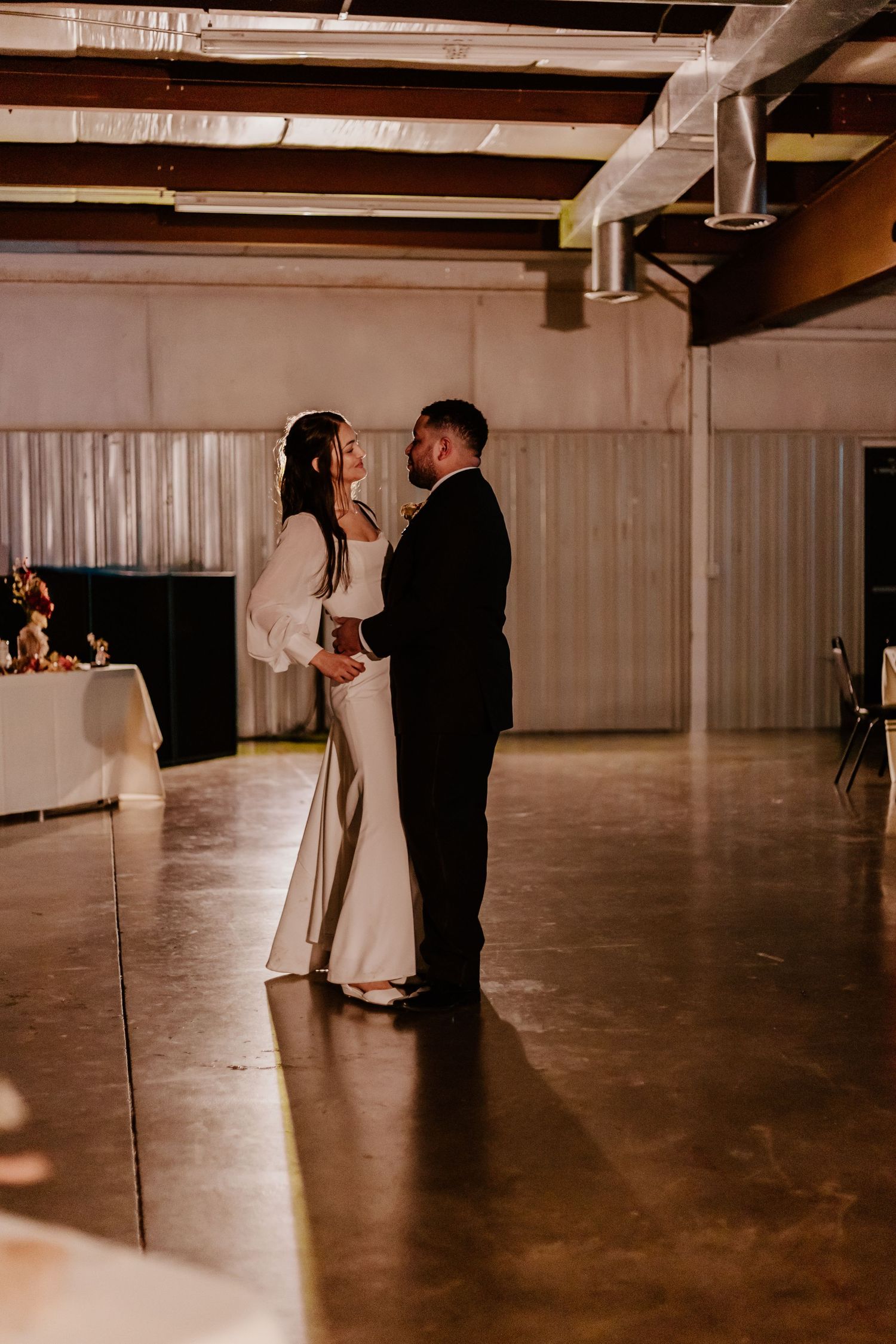 Couple dancing together in an empty warehouse space with dramatic lighting and shadows.