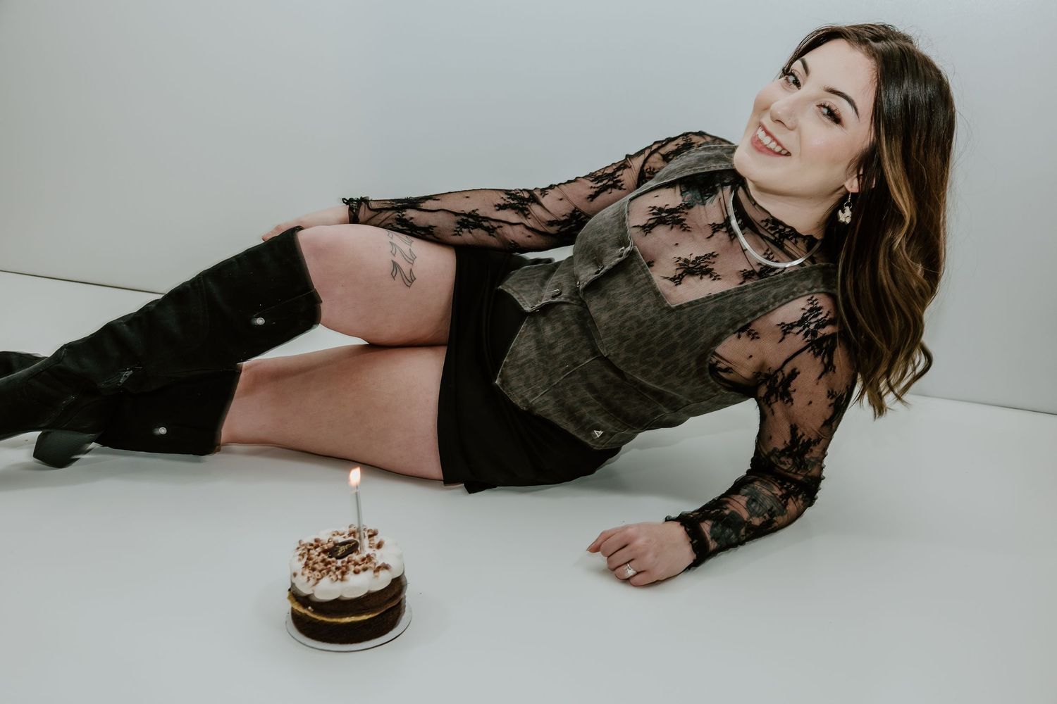 Person in black lace lingerie poses seductively on white floor in artistic boudoir photoshoot series.