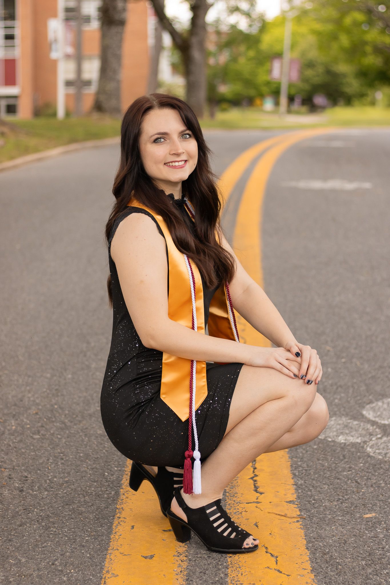A person sits on a yellow road line wearing a black top and boots during an urban outdoor photoshoot.