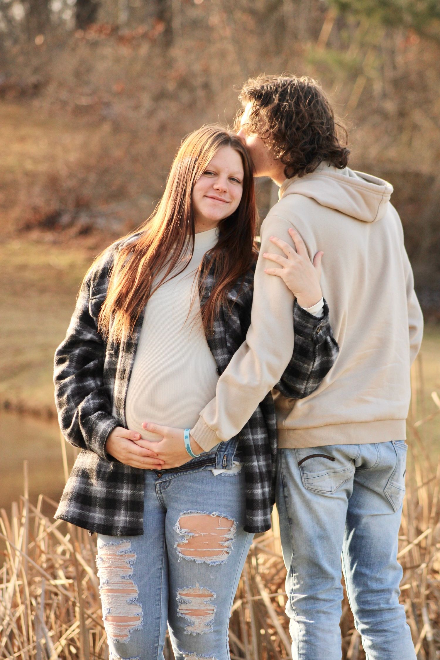 Couple wearing casual denim and plaid clothing embracing outdoors in a natural autumn setting.