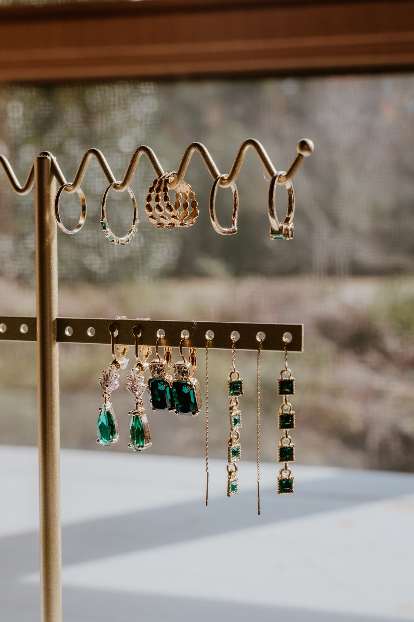 Multiple pairs of delicate dangle earrings with emerald green stones and gold accents displayed on a jewelry stand.