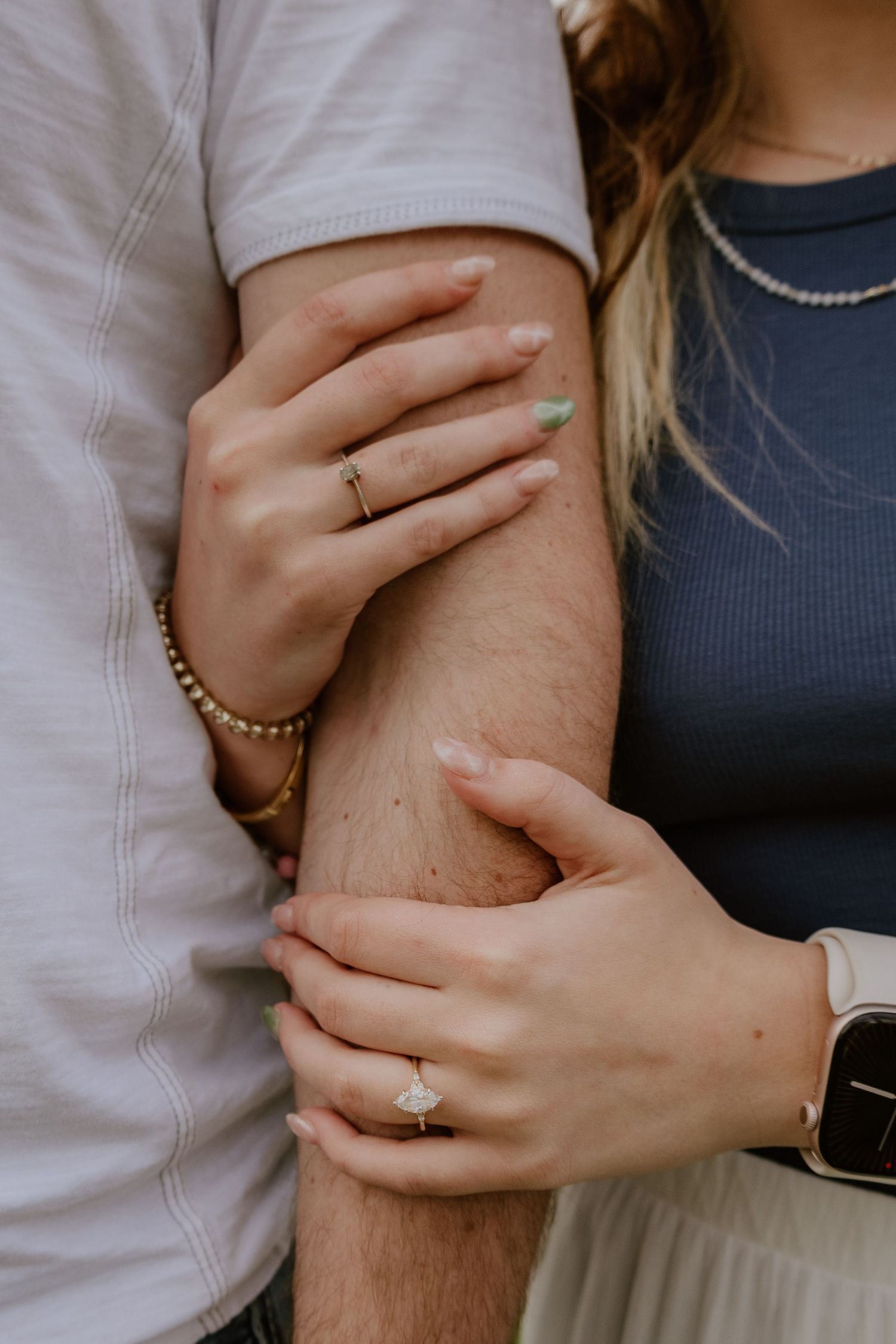 Close-up shot of hands wearing an engagement ring and Apple Watch against a light gray background.