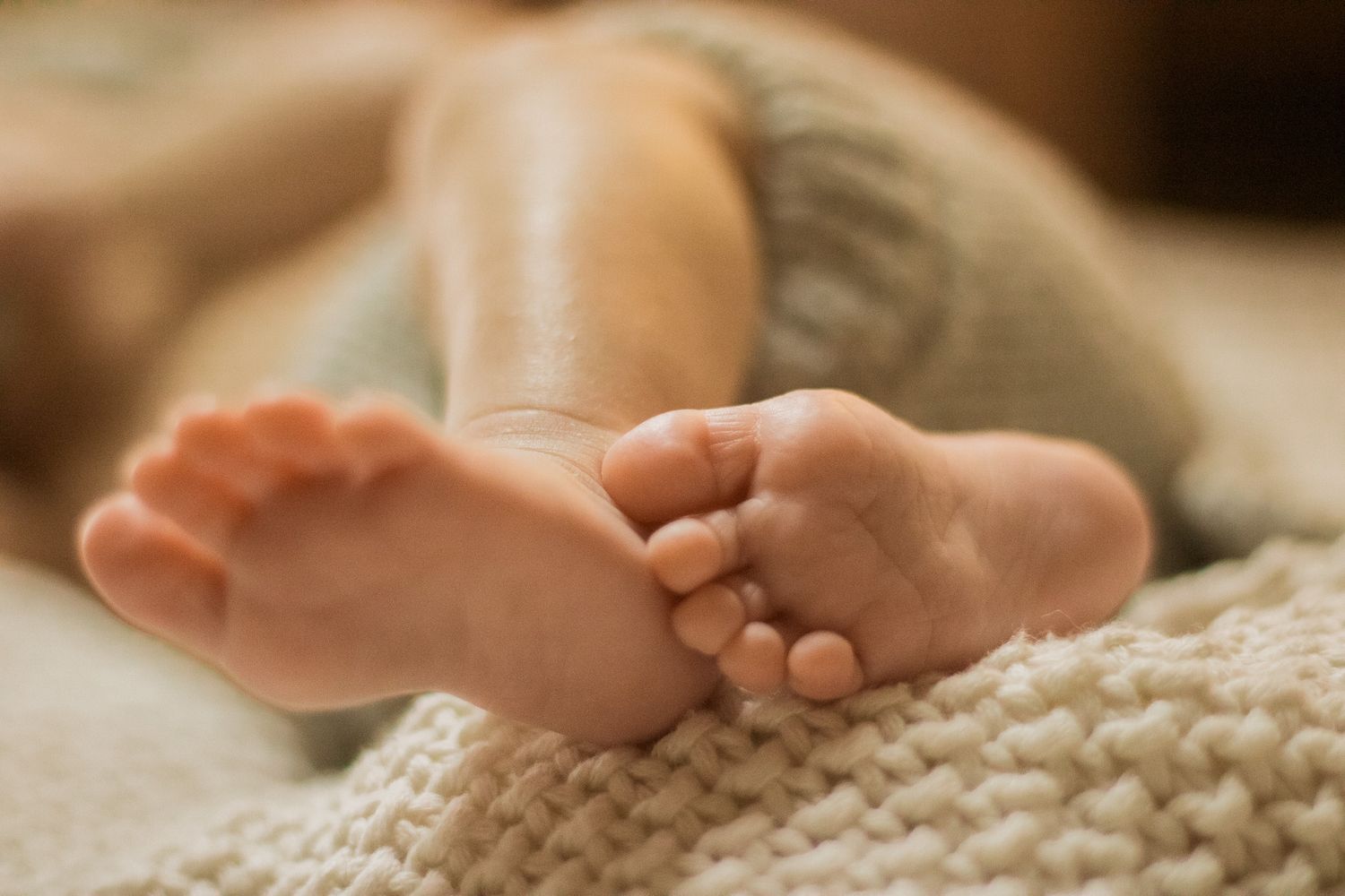 Close-up of tiny baby feet resting on textured knit blanket in warm lighting.