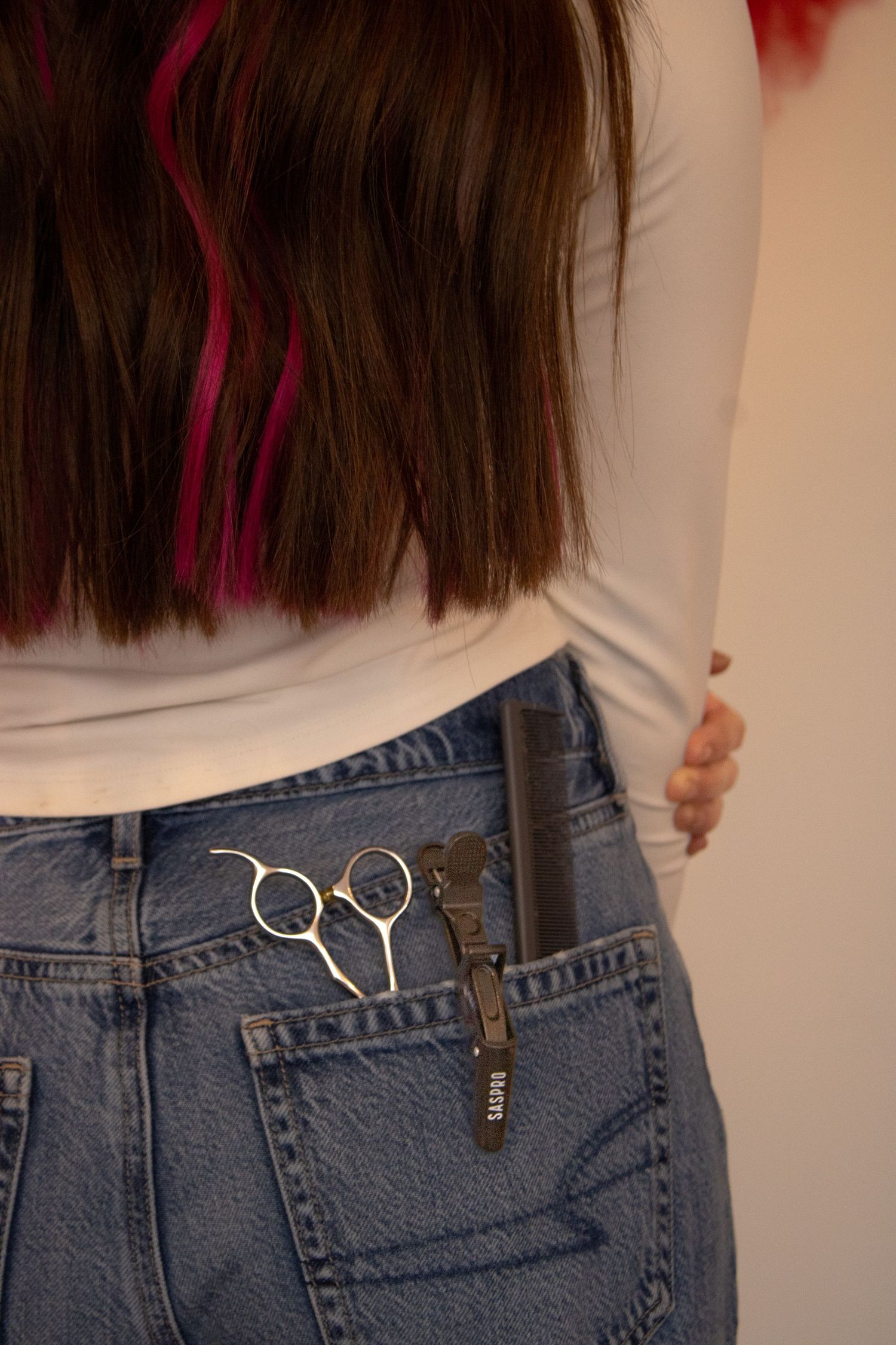 Close-up of denim jeans with scissors hanging from belt loop showing DIY fashion styling technique.