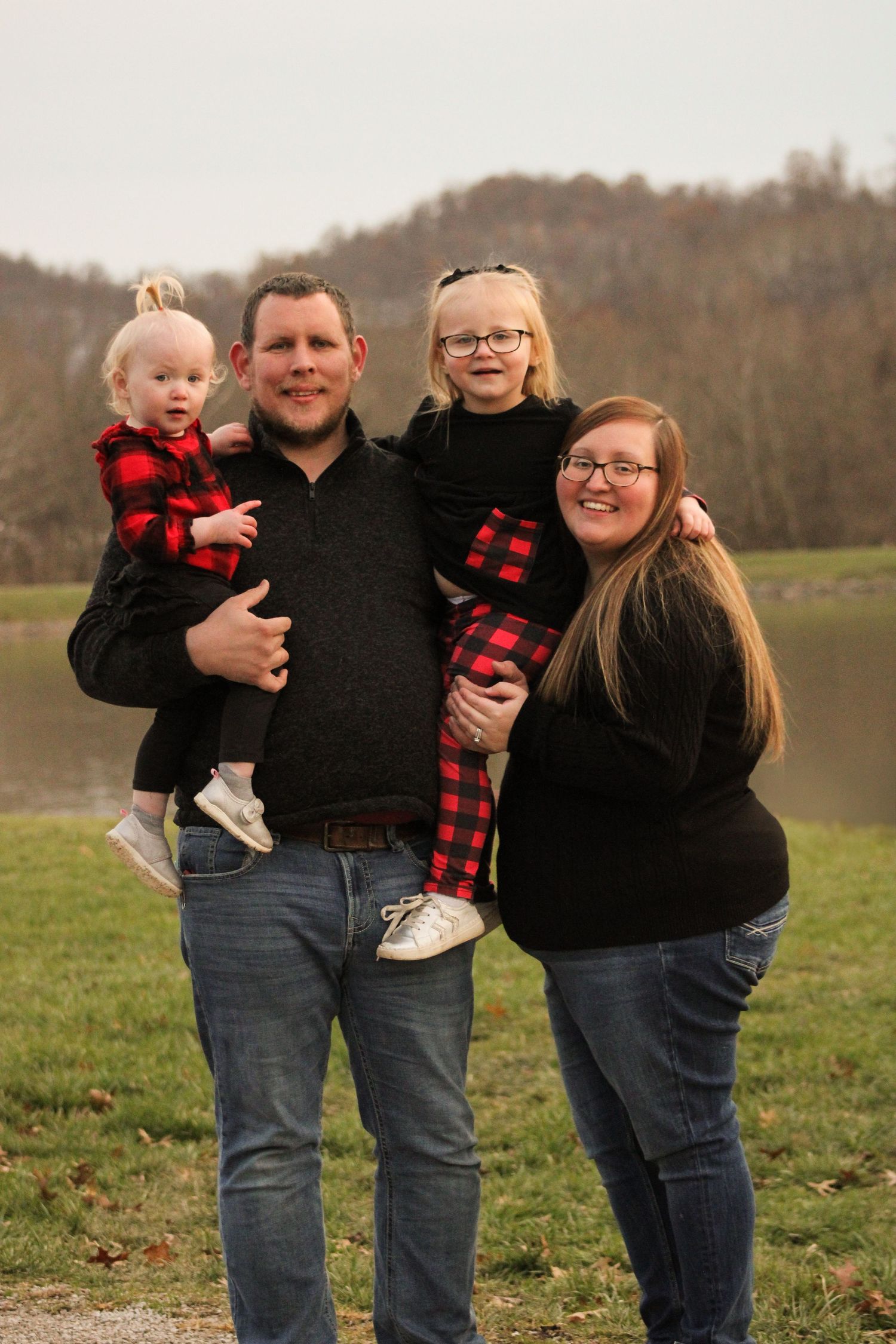 Family wearing coordinating black and red buffalo plaid outfits poses together in a grassy field.