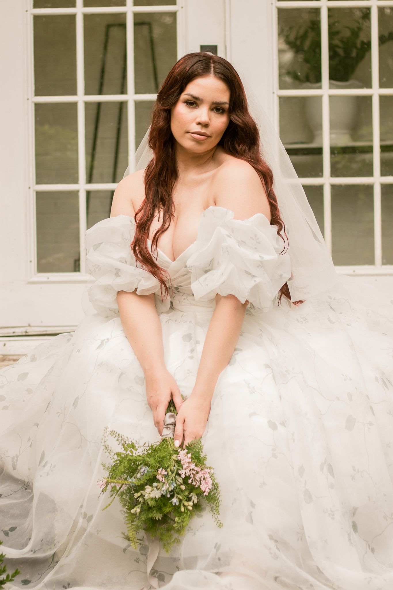 Dreamy bridal session with delicate bouquet and voluminous white dress in front of classic white windows.
