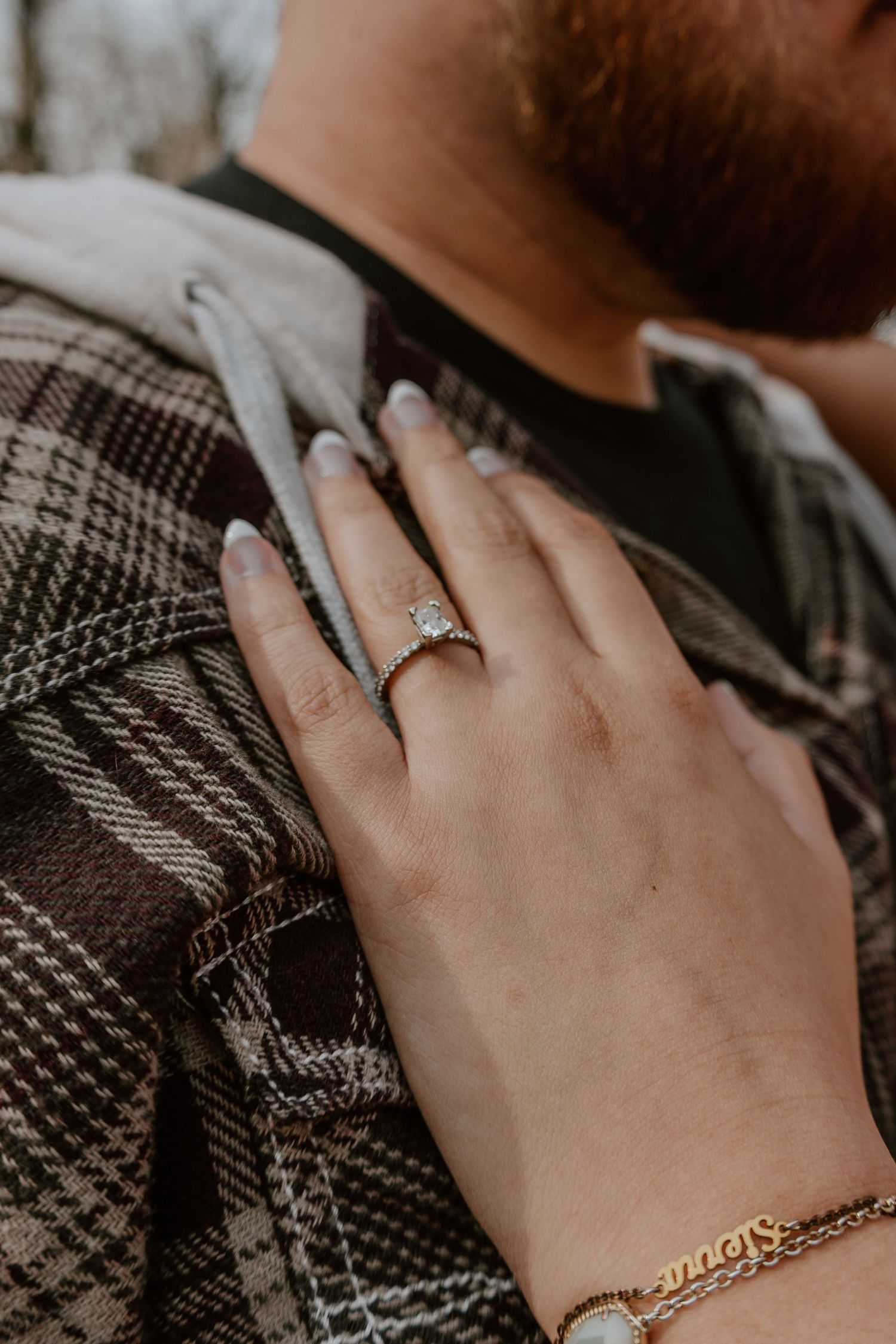 Close-up shots of hands wearing elegant engagement rings against a dark plaid fabric background.