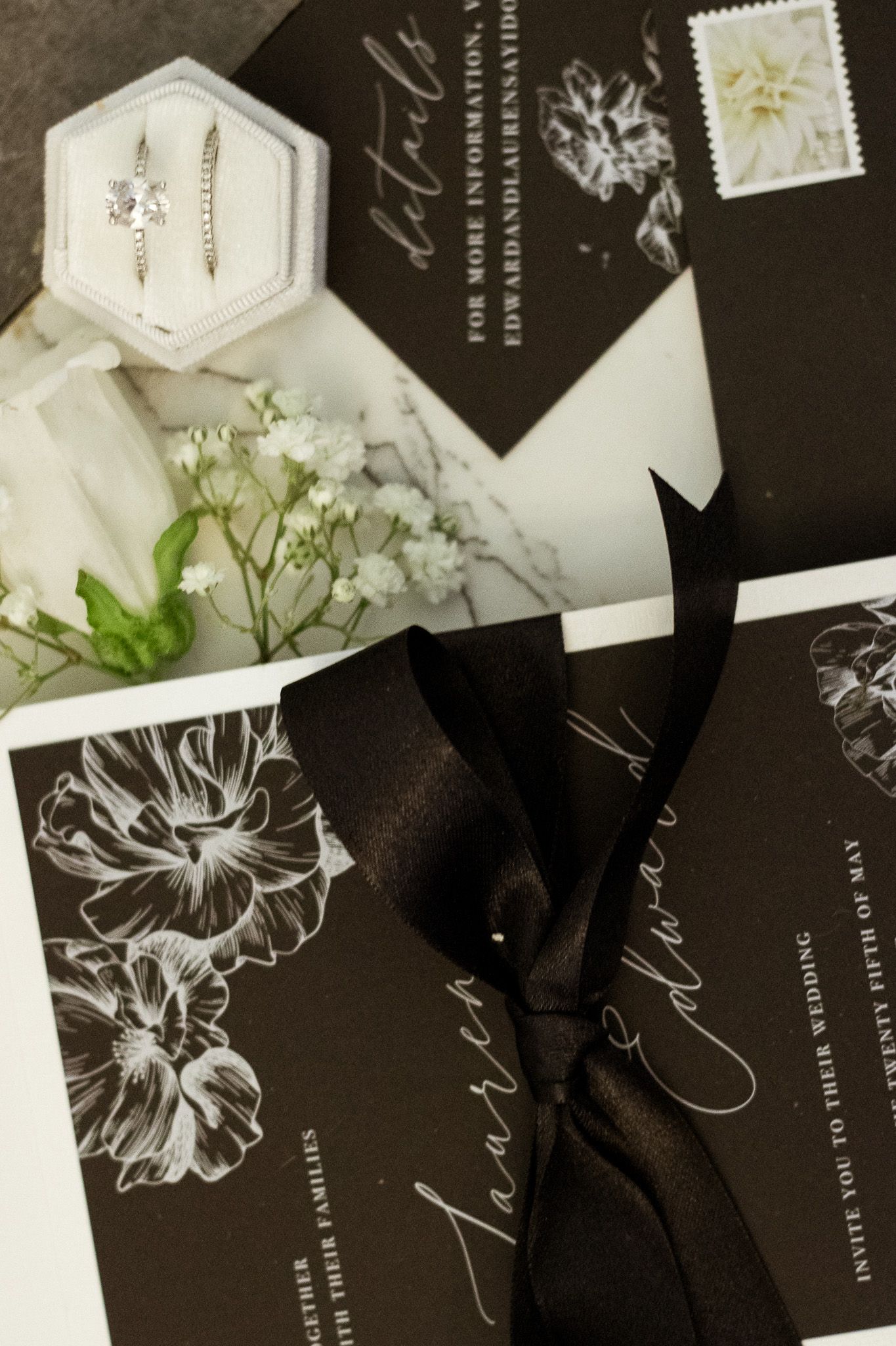 Black and white wedding invitations with elegant floral designs and white envelopes arranged on dark background.