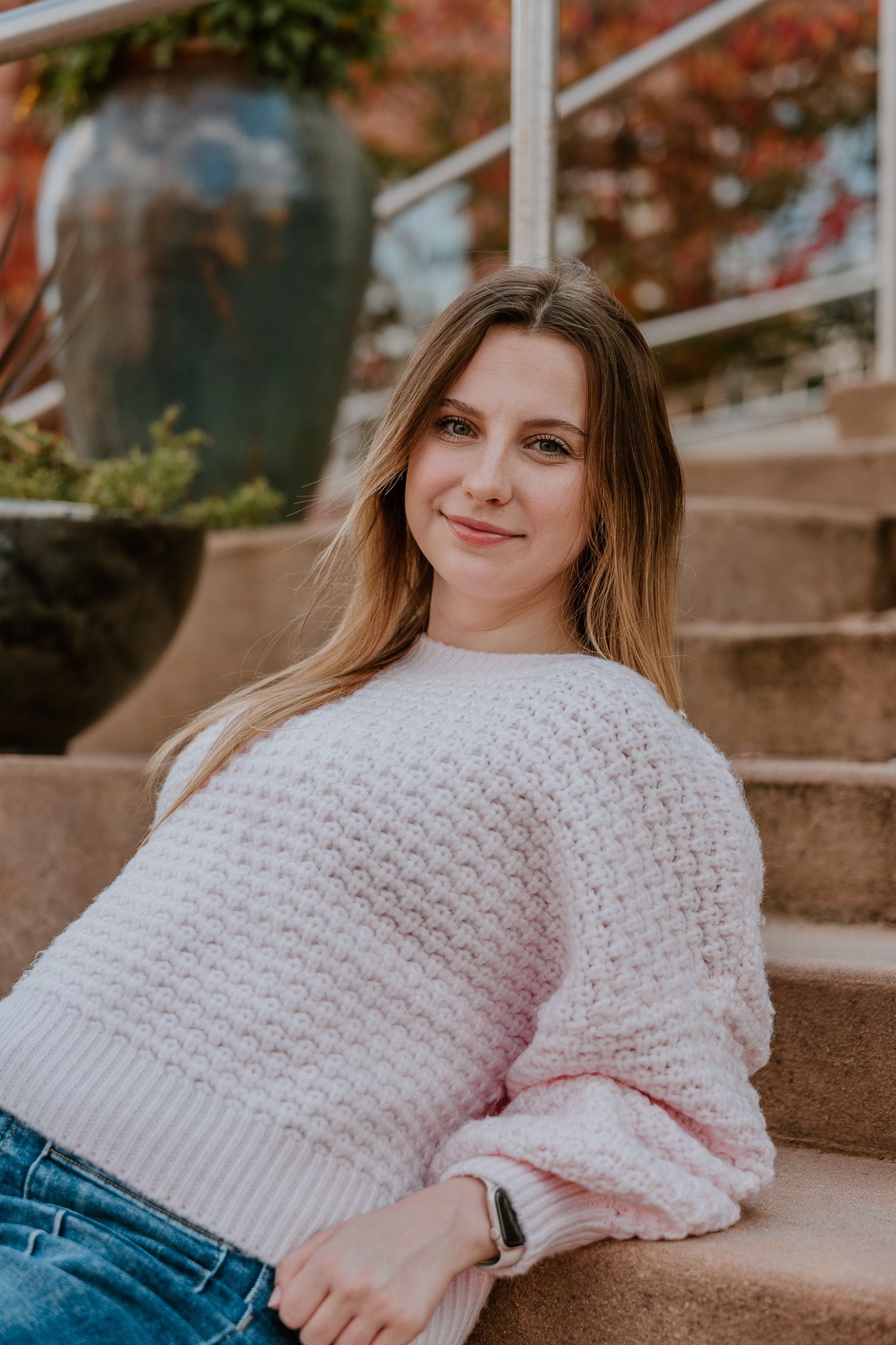 A person in a cozy pink knit sweater and jeans sits on concrete steps during autumn.