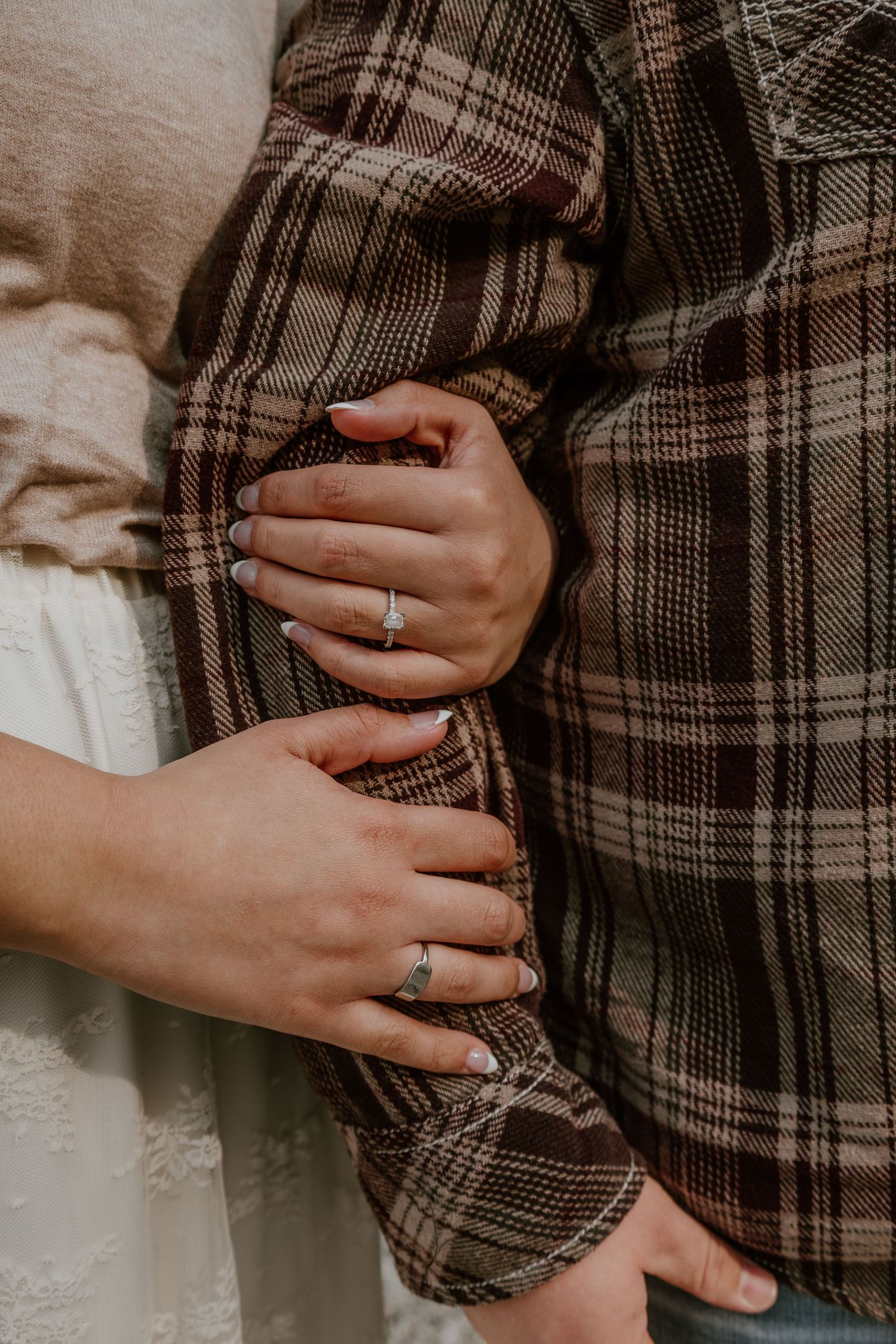 Close-up view of hands wearing a silver ring against a brown plaid fabric background.